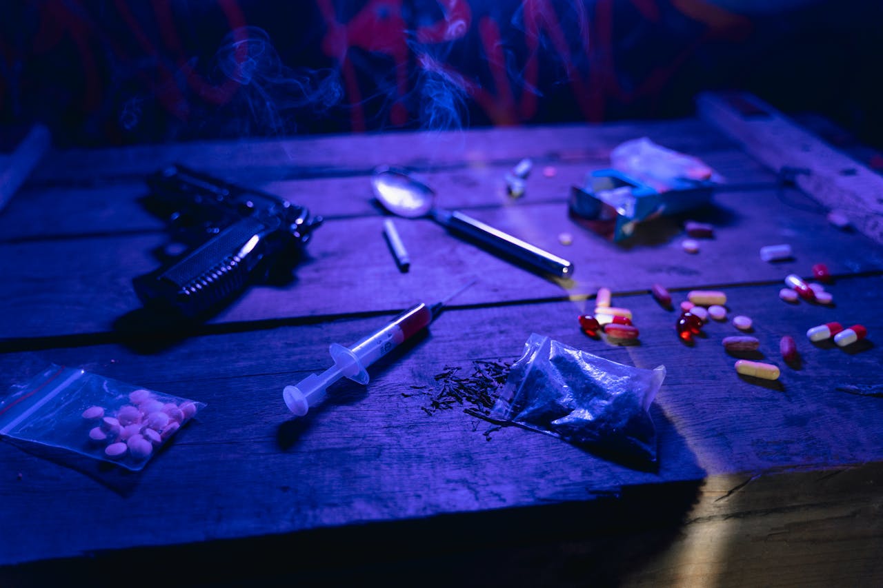 A moody scene displaying drugs, a gun, and smoke under dramatic lighting.
